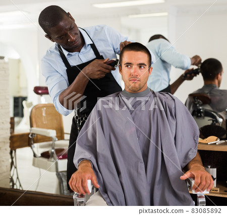 Man getting haircutting by African barber 83085892