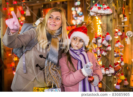 Happy daughter with mom point finger at selected christmas tree decorations at street market Happy daughter with mom point finger at selected christmas tree decorations at street market 83085905