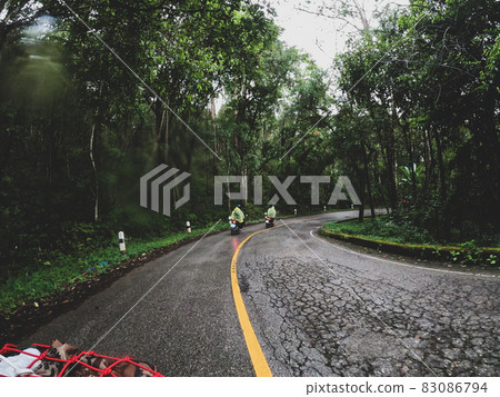 View while riding a motorcycle on a mountain road in the rainforest in the rainy season. Biker is riding a motorcycle on the road. View while riding a motorcycle on a mountain road in the rainforest in the rainy season. Biker is riding a motorcycle on the road. 83086794