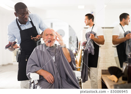 Senior man unpleasantly surprised by haircut from African hairdresser 83086945