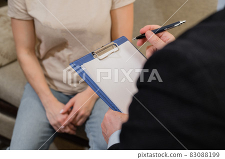 An elderly male psychotherapist talking to a female patient and taking notes on a clipboard. Close-up of the hands of a male psychologist 83088199