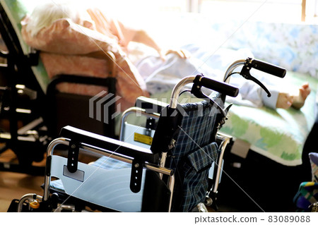 斜倚在護理床上的老年婦女和輪椅 83089088