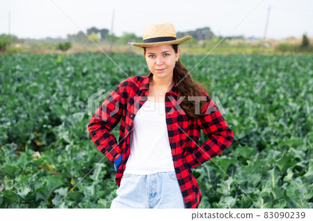 Portrait of young woman farmer in straw hat posing in farm field 83090239