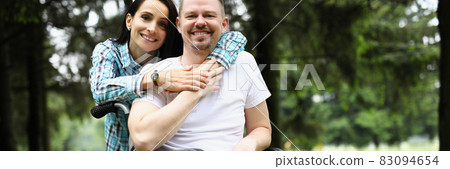Young woman hugs disabled man in wheelchair on walk in park 83094654