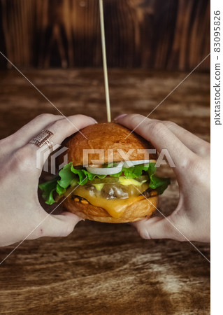 Close-up of a standard burger. Adult fast food in a restaurant or cafe. Macro photo of burger ingredients with meat, cheese and herbs. Eco burgers for the whole family 83095826