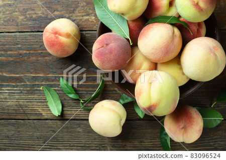 Ripe peaches in a clay plate on a wooden table with scattered leaves. 83096524