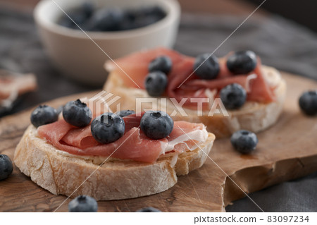 Bruschetta with prosciutto with cream cheese and blueberries on olive wood board Bruschetta with prosciutto with cream cheese and blueberries on olive wood board 83097234