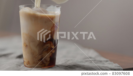 milk pour cold in brew coffee in tumbler glass on walnut table milk pour cold in brew coffee in tumbler glass on walnut table 83097608