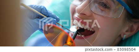 Doctor dentist treating teeth using LED curing light machine in clinic closeup 83098504