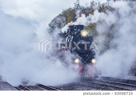 Retro steam train departs from the station wooden platform. Retro steam train departs from the station wooden platform. 83098710