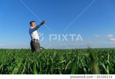 businessman poses in a field, he looks into the distance and rests, green grass and blue sky as background businessman poses in a field, he looks into the distance and rests, green grass and blue sky as background 83100119