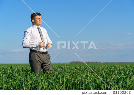 businessman poses in a field, he looks into the distance, green grass and blue sky as background businessman poses in a field, he looks into the distance, green grass and blue sky as background 83100268