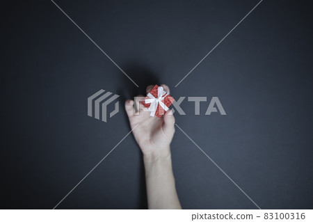 Women's fingers are holding a tiny red shiny box with a white bow. Top view. Holiday gift Women's fingers are holding a tiny red shiny box with a white bow. Top view. Holiday gift 83100316
