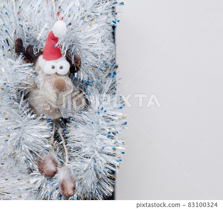 A funny toy deer with bulging eyes lies in silver tinsel. Christmas decor. Top view 83100324