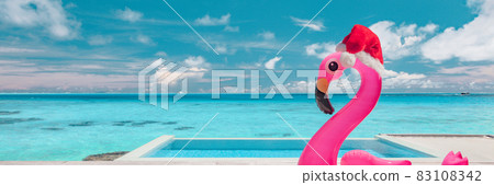 Christmas travel holidays beach destination banner funny pool flamingo with Santa hat at luxury south winter destination during Xmas. Landscape header background Christmas travel holidays beach destination banner funny pool flamingo with Santa hat at luxury south winter destination during Xmas. Landscape header background 83108342