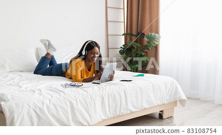 Black Woman Using Tablet Wearing Earphones Learning In Bedroom, Panorama Black Woman Using Tablet Wearing Earphones Learning In Bedroom, Panorama 83108754