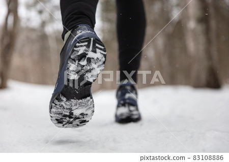 Winter exercise fitness lifestyle athlete walking with running shoes on snow and slippery ice needing traction soles on icy sidewalks. Run outside in cold weather 83108886