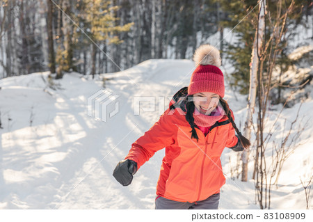 Happy Asian woman laughing walking in snow forest during winter. Beautiful portrait of young adult smiling wearing cold weather hat and gloves, orange jacket Happy Asian woman laughing walking in snow forest during winter. Beautiful portrait of young adult smiling wearing cold weather hat and gloves, orange jacket 83108909