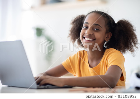 Cheerful black girl studying online, using laptop, typing on keyboard Cheerful black girl studying online, using laptop, typing on keyboard 83108952