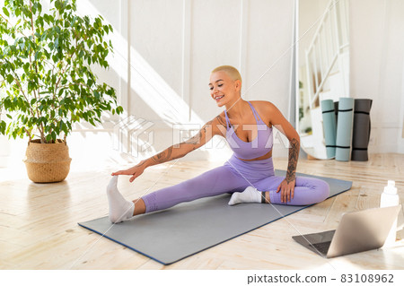 Home training. Young caucasian woman stretching leg muscles in front of laptop, watching video tutorials online 83108962