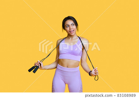 Sport for every body. Fit black woman holding skipping rope, posing in sportswear over yellow background, free space 83108989
