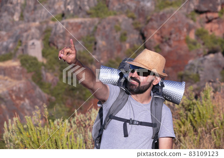 Hispanic male trekker with sunglasses smiling and pointing out of the frame Hispanic male trekker with sunglasses smiling and pointing out of the frame 83109123