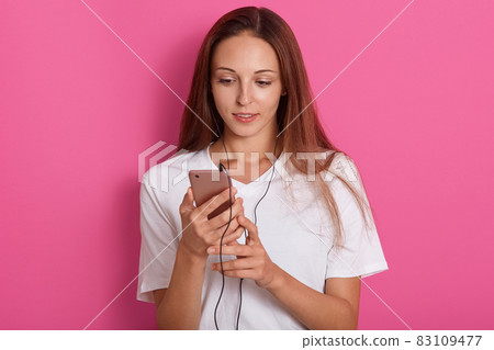 Young woman using her modern mobile cellphone, touching the screen with finger, posing over rosy background, wearing white t shirt, having beautiful staright hair, listening to music, relaxing at home Young woman using her modern mobile cellphone, touching the screen with finger, posing over rosy background, wearing white t shirt, having beautiful staright hair, listening to music, relaxing at home 83109477
