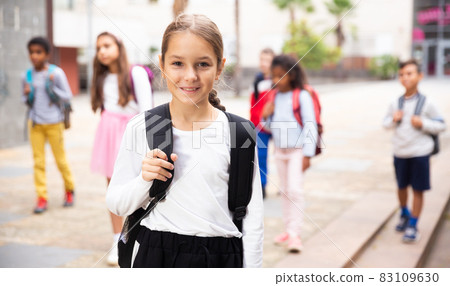 Positive schoolgirl standing near school, children on background Positive schoolgirl standing near school, children on background 83109630