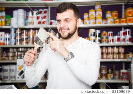 cheerful male customer examining various types of brushes in paint store cheerful male customer examining various types of brushes in paint store 83109689