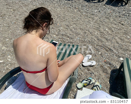 Rear View Of Woman Looking At Sea While Sitting Against Sky Rear View Of Woman Looking At Sea While Sitting Against Sky 83110457