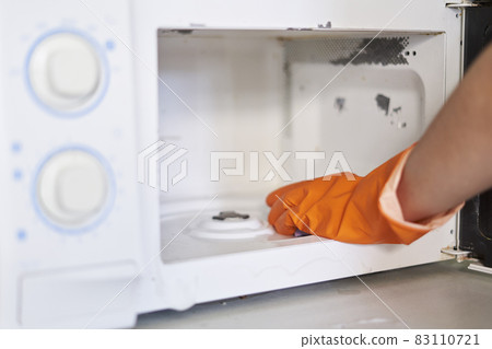 Woman in rubber gloves cleaning microwave oven with sponge in kitchen. Cleaning microwave in the kitchen 83110721