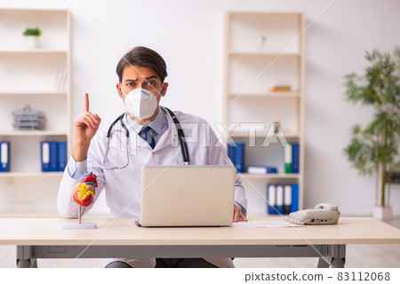 Young male doctor cardiologist working in the clinic during pand Young male doctor cardiologist working in the clinic during pand 83112068