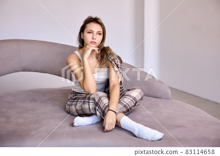 Slim woman in home suit sits on bed in bedroom. 83114658