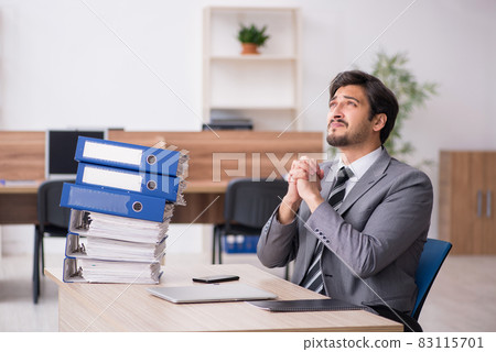 Young male employee unhappy with excessive work in the office Young male employee unhappy with excessive work in the office 83115701