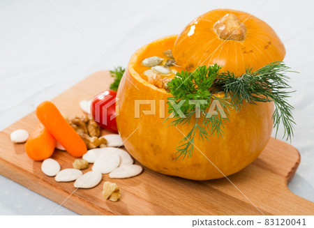 Tasty homemade pumpkin soup puree served in pumpkin at wooden desk 83120041