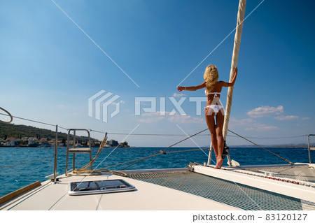 Woman in bikini tanning and relaxing on a summer catamaran sailing cruise 83120127