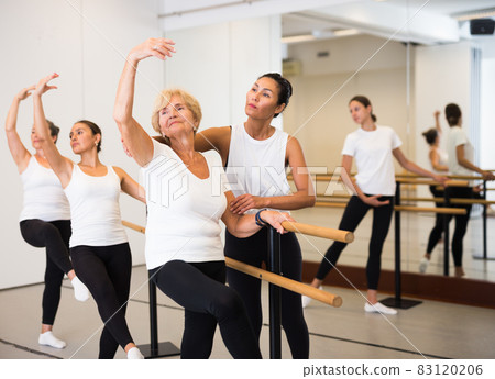 Various aged women exercising ballet moves with trainer 83120206