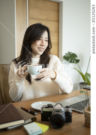 Portrait of smiling young woman in sweater sitting in office room and drinking hot coffee. Portrait of smiling young woman in sweater sitting in office room and drinking hot coffee. 83120263