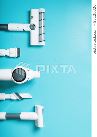 A set of nozzles and a white cordless vacuum cleaner in a row on a blue background, free space. Top view 83120326