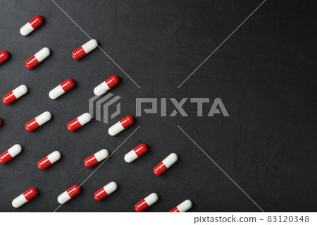 A pattern of red and white pill capsules on a black background background. 83120348