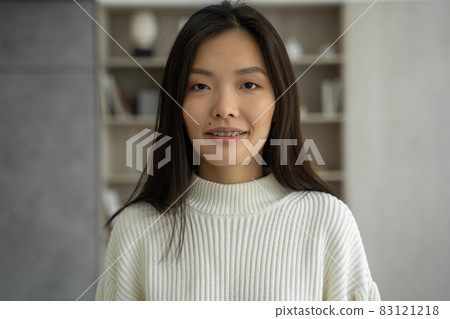 Asian woman feels happy, smiles and looks at the camera standing in her living room Asian woman feels happy, smiles and looks at the camera standing in her living room 83121218