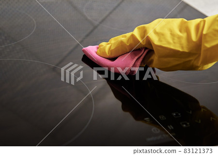 Woman in rubber gloves cleaning induction stove 83121373