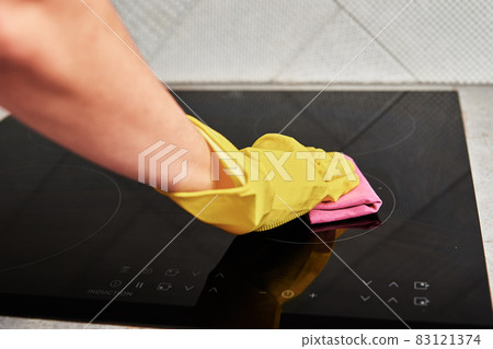Woman in rubber gloves cleaning induction stove 83121374