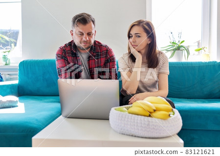 Serious middle aged couple looking at laptop screen at home in living room 83121621