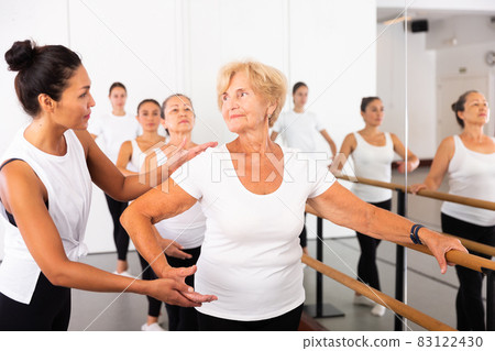 Various aged women exercising ballet moves with trainer 83122430