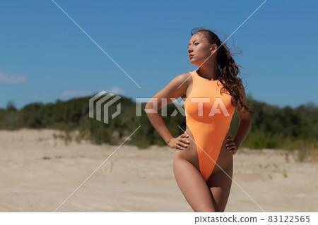 Young woman in orange swimsuit standing on sand Young woman in orange swimsuit standing on sand 83122565
