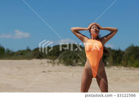 Young woman in orange swimsuit standing on sand 83122566