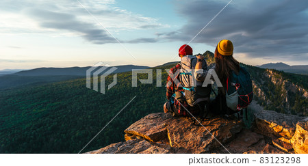 A happy couple in the mountains admires the beautiful views. A man and a woman with backpacks on the mountain admire the panoramic view. Travelers enjoy climbing the mountain at sunset. Copy space A happy couple in the mountains admires the beautiful views. A man and a woman with backpacks on the mountain admire the panoramic view. Travelers enjoy climbing the mountain at sunset. Copy space 83123298