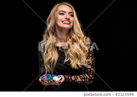 Elegant blonde in a black dress, casino player holding a handful of chips on black background Elegant blonde in a black dress, casino player holding a handful of chips on black background 83123594