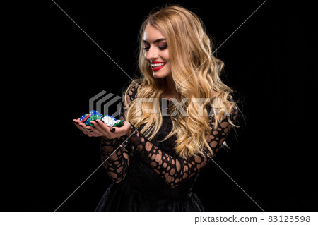 Elegant blonde in a black dress, casino player holding a handful of chips on black background Elegant blonde in a black dress, casino player holding a handful of chips on black background 83123598